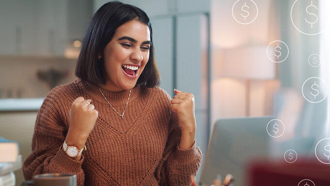 Women seated at lap top celebrating what she sees, dollar sign graphics are imposed over photo