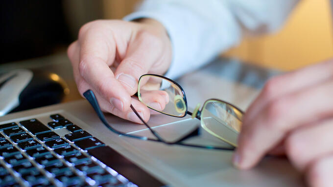 Close-up of a man's hands holding glasses above a laptop keyboard