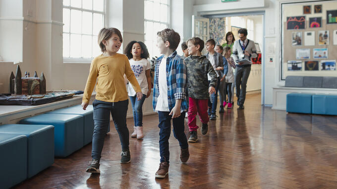Elementary aged kids walking down a hall with teachers following behind