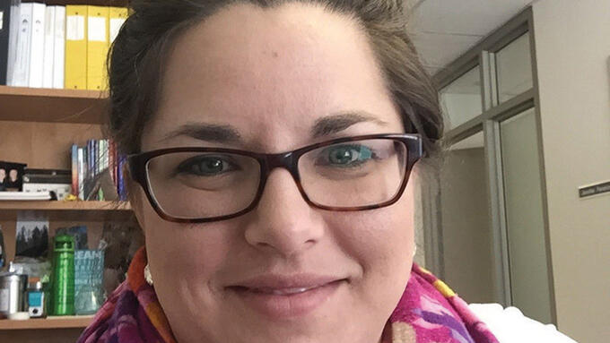 Portrait of white brunet women wearing glasses and pink scarf and with her hair pulled into a top bun. 