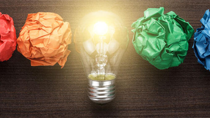 Paper in a rainbow of colours crunched into balls in a line, in the middle an illuminated light bulb