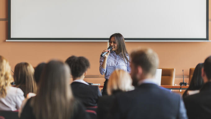 Young women of colour speaking to an audience in front of a white board