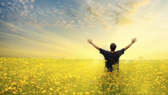 Man standing with his arms raised in a yellow field