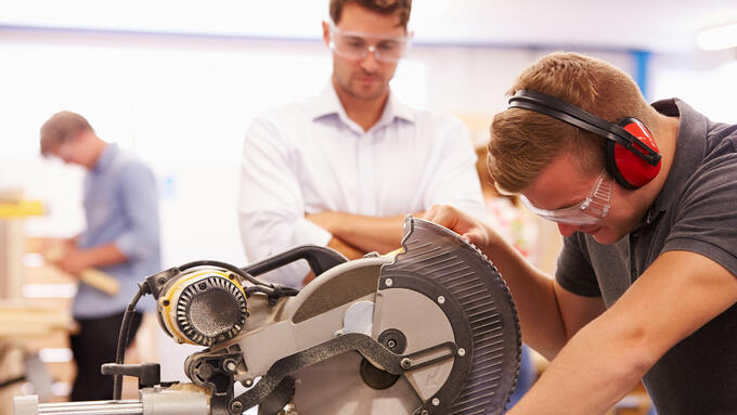 Man looking over student using saw