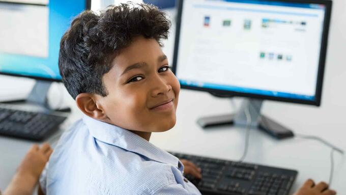 School boy sitting at a computer looking behind his shoulder