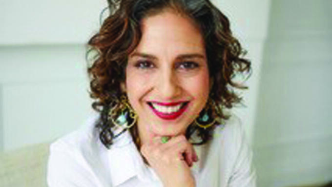 A photo of a brunette woman with her hand under her chin seated at a desk