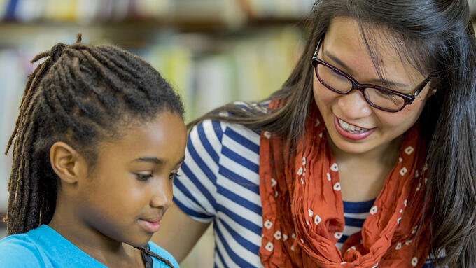 A teacher sits with a student at a desk