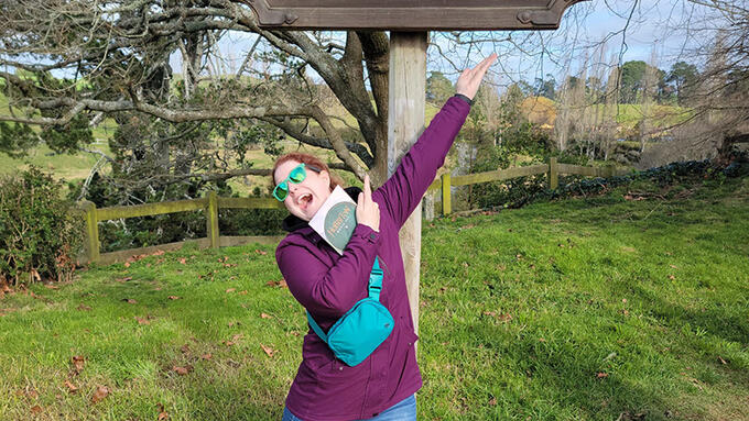 A woman standing in front of a sign that says Hobbiton