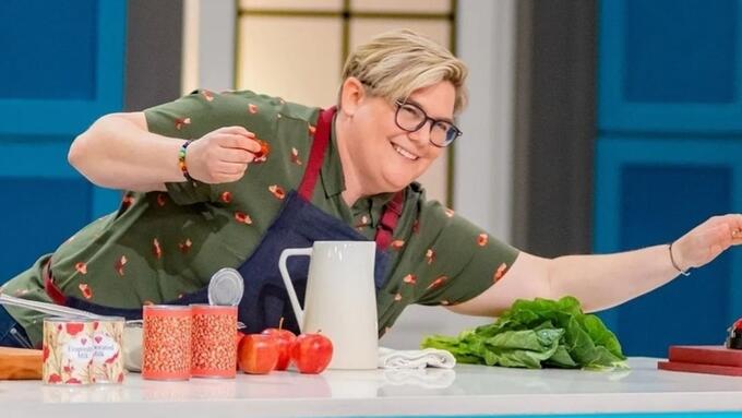 Contestant in a tv cooking show reaches across a counter with an apron on
