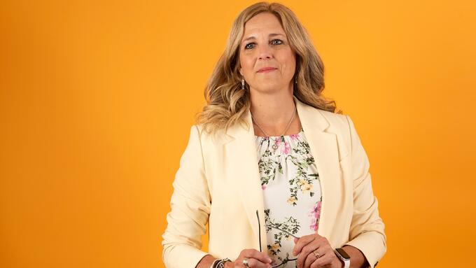 Krimsen Sumners wearing a beige blazer in front of orange background