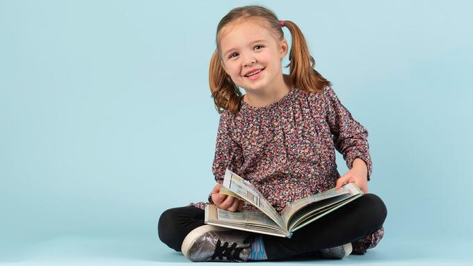 Young girl with pigtails sitting cross-legged with a book 