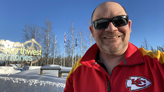 Man wearing a red coat poses in front of Northwest Territories sign on a clear winter day