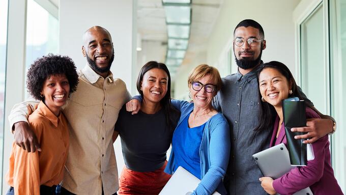 Diverse smiling adults standing with arms around each other in a hallway