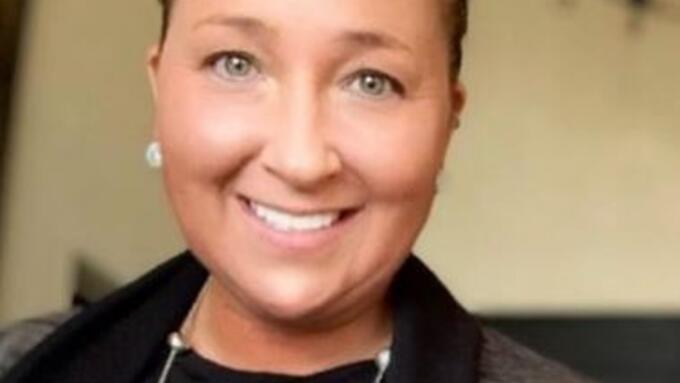 A woman with hair tied back wearing a black blouse and a gray jacket with matching earings and necklace