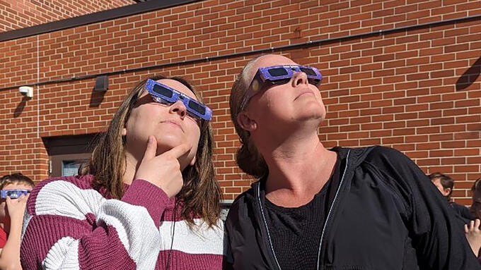 Two women look at the solar eclipse through protective glasses