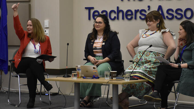 Four women sit on a panel at the front of a conference presentation