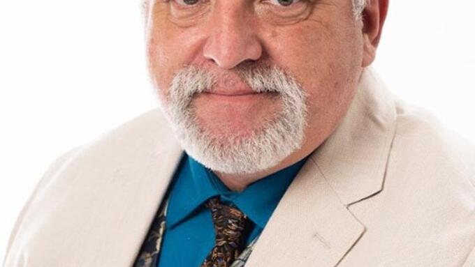 Man with a grey goatee, white suit and a matching paisley tie and vest