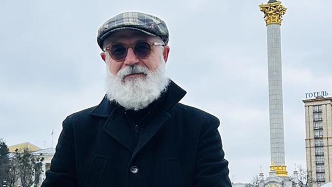 Man in a plaid cap and white beard stands infront of Independence Monument in Kyiv 