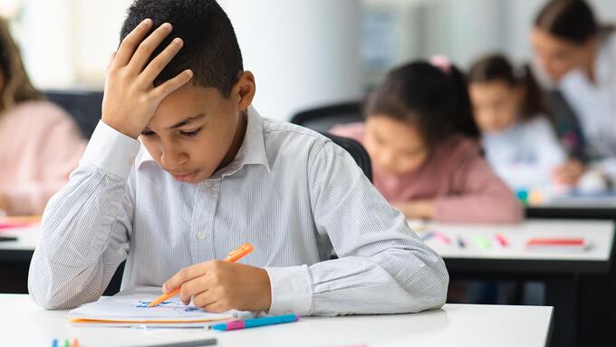 Boy at desk with head in hand as he looks down at classwork