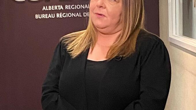 women in black blazer holding a sheet of paper infront of the CUPE logo