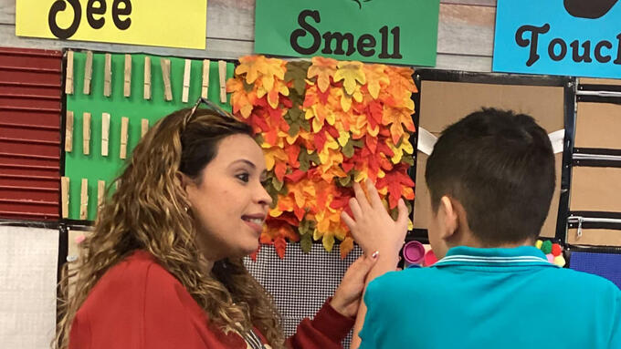 Teacher guides a student's hand over a sensory wall