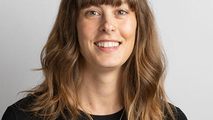 Young women with long brown hair and bangs wearing a black shirt, pendant necklace