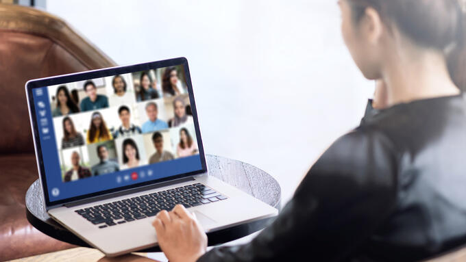 A person wearing a black blouse sitting in front of a laptop screen that has 15 faces on it, all people part of an online meeting