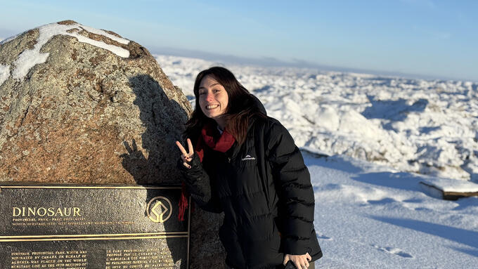 A woman stands beside a plaque on top of a mountain
