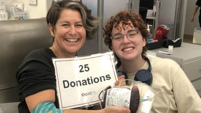 Teacher with a student at a blood donation center holding a 25 donations sign