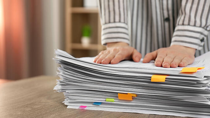 A teacher's hands set on top of a stack of paper with colourful sticky tabs.