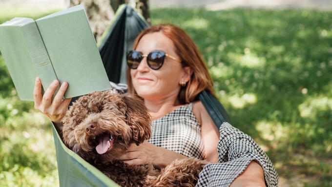 Women laying in a hammock reading a book with her doodle dog
