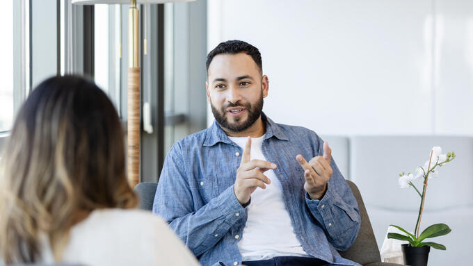 Young man with beard wearing a denim shirt talks with a women in a white shirt
