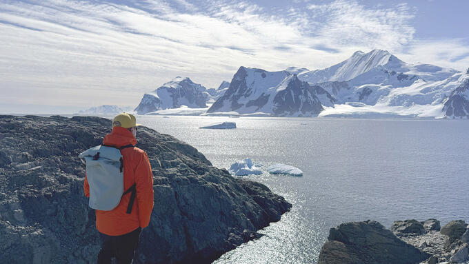 A man stands on a rocky shore looking at out icebergs 