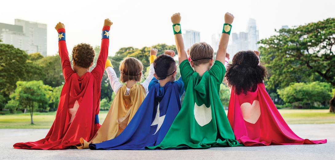 5 children faced away from the camera wearing different coloured superhero capes with hearts, lightning bolts and shields on the back.