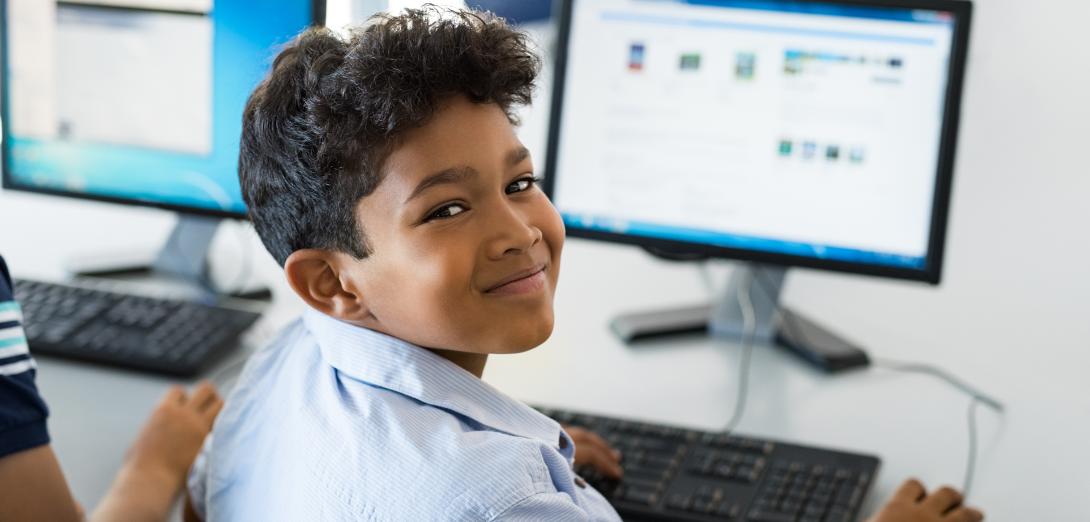 School boy sitting at a computer looking behind his shoulder