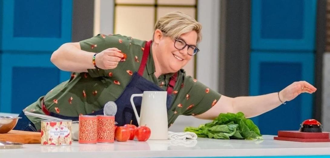 Contestant in a tv cooking show reaches across a counter with an apron on