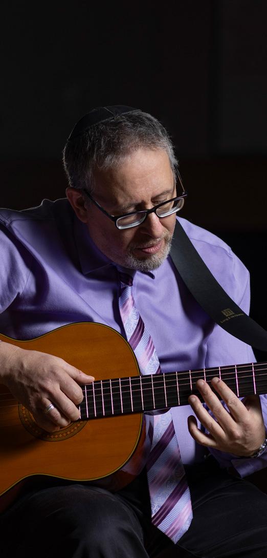 A person in glasses and a purple shirt and tie playing a guitar