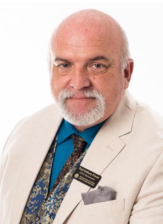 Man with a grey goatee, white suit and a matching paisley tie and vest