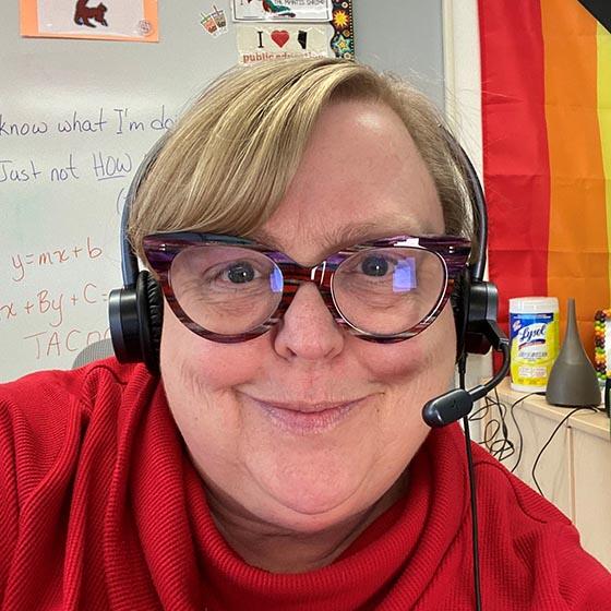 Women with short blond hair wearing glasses, a headset and red sweater.