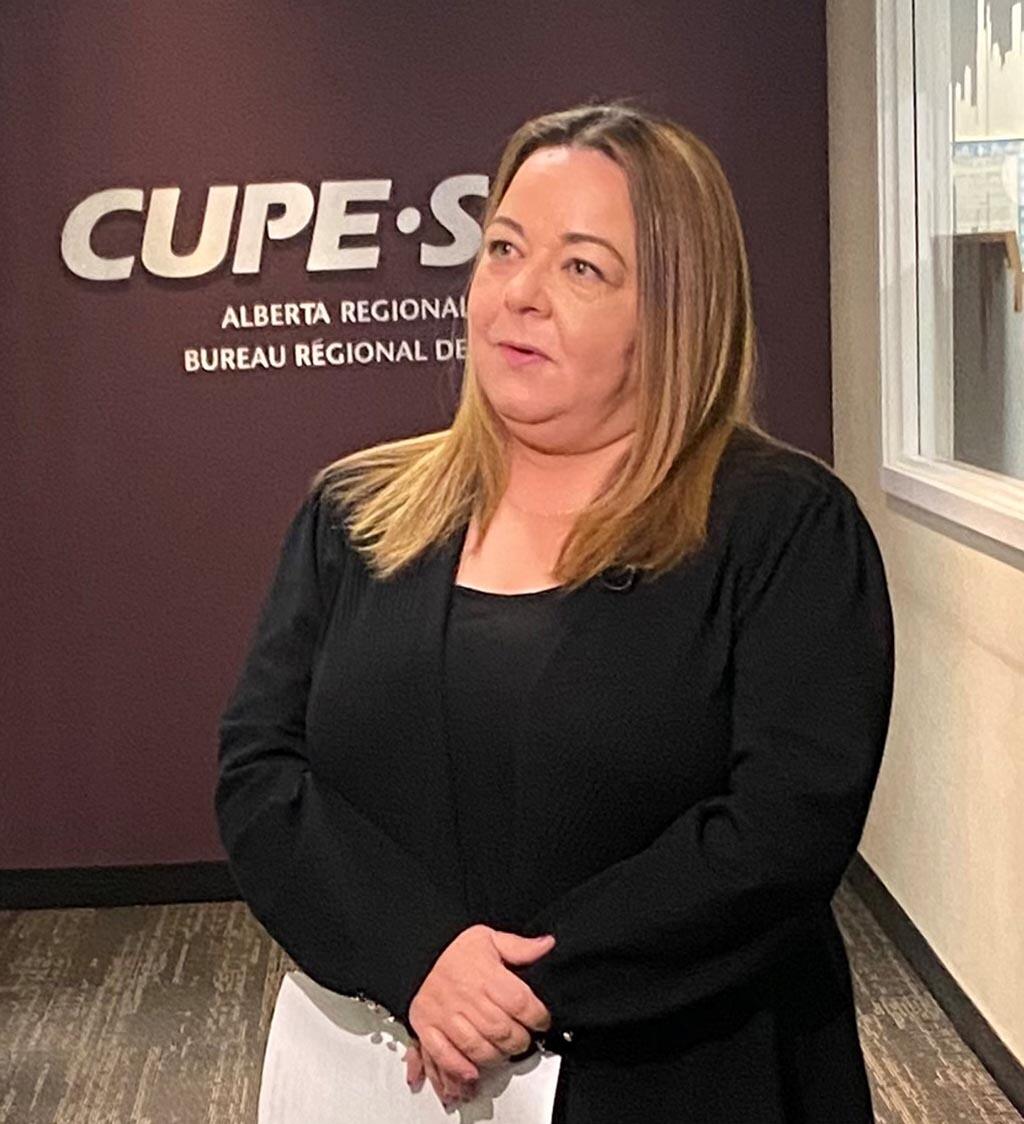 women in black blazer holding a sheet of paper infront of the CUPE logo