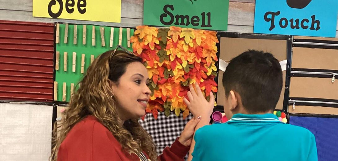 Teacher guides a student's hand over a sensory wall