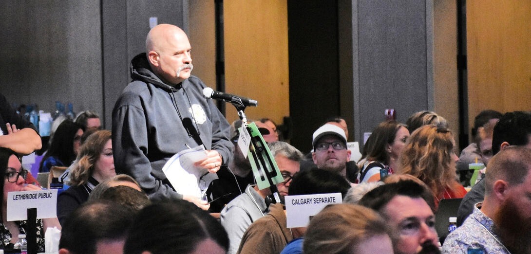 Bald man in a grey hoodie standing in a crowd at a microphone