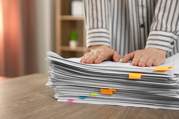 A teacher's hands set on top of a stack of paper with colourful sticky tabs.