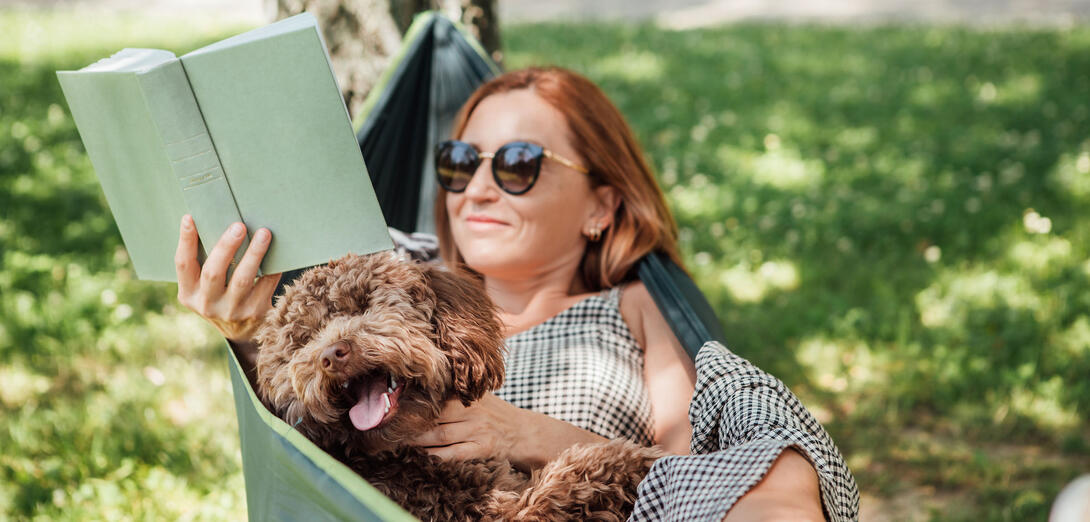Women laying in a hammock reading a book with her doodle dog