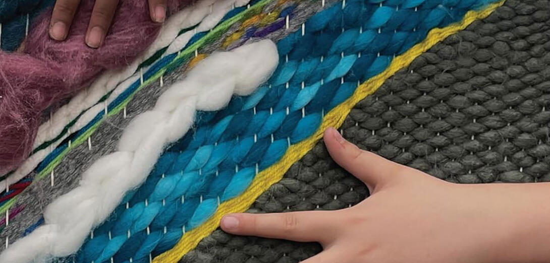 Kids hands feeling a woven fabric with many colours and textures